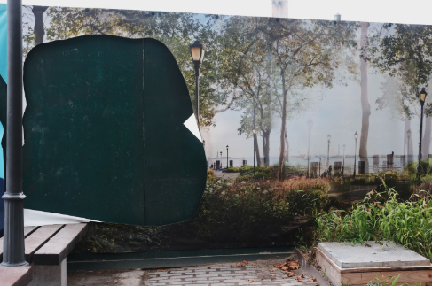 A large peeling advertisement of a park scene featuring trees and a waterfront reveals a dense green wooden fence temporarily established. Small green plants and a bench adjacent to the fence add to its trompe l'oeil effect.